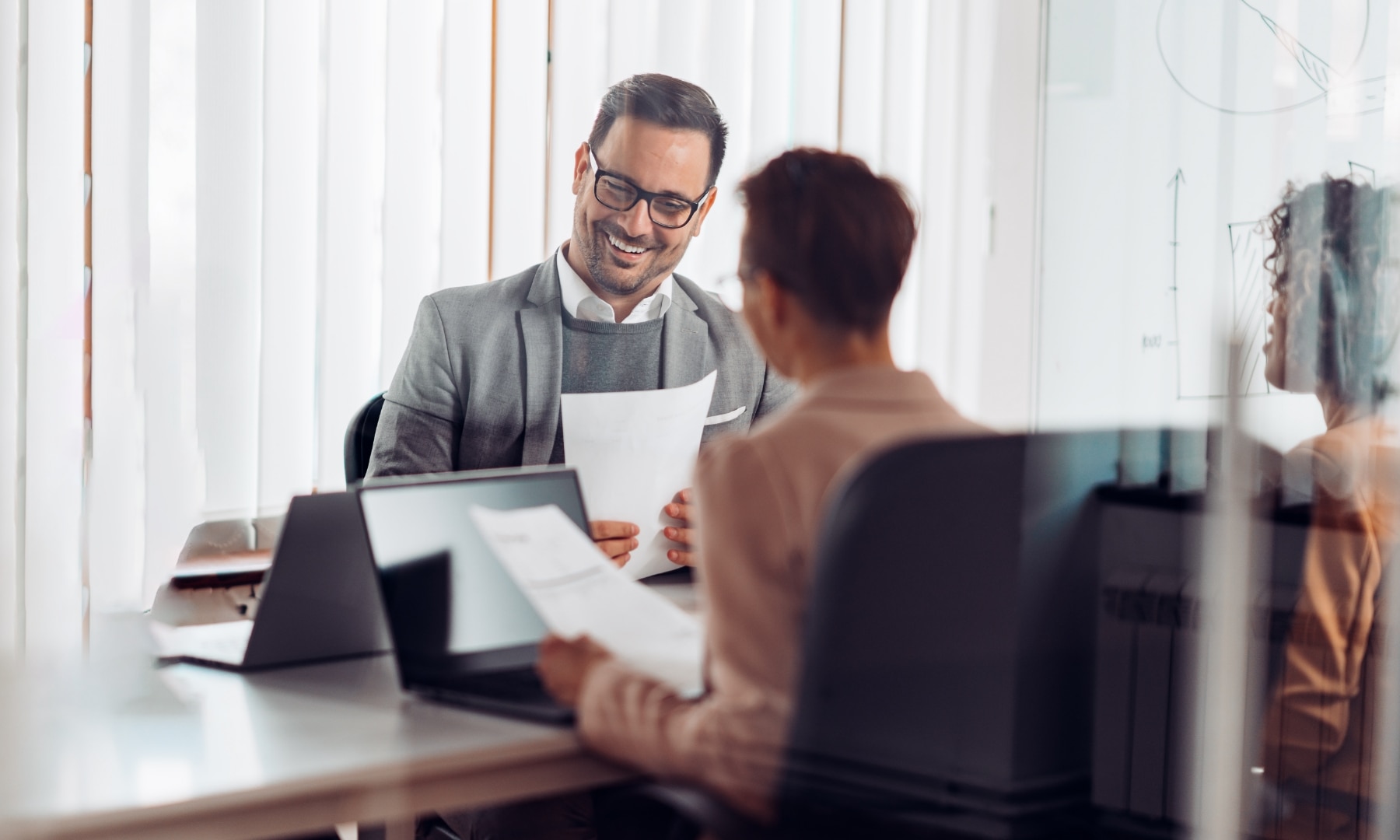 A woman and a man in a conference room reviewing paperwork and laptop screens