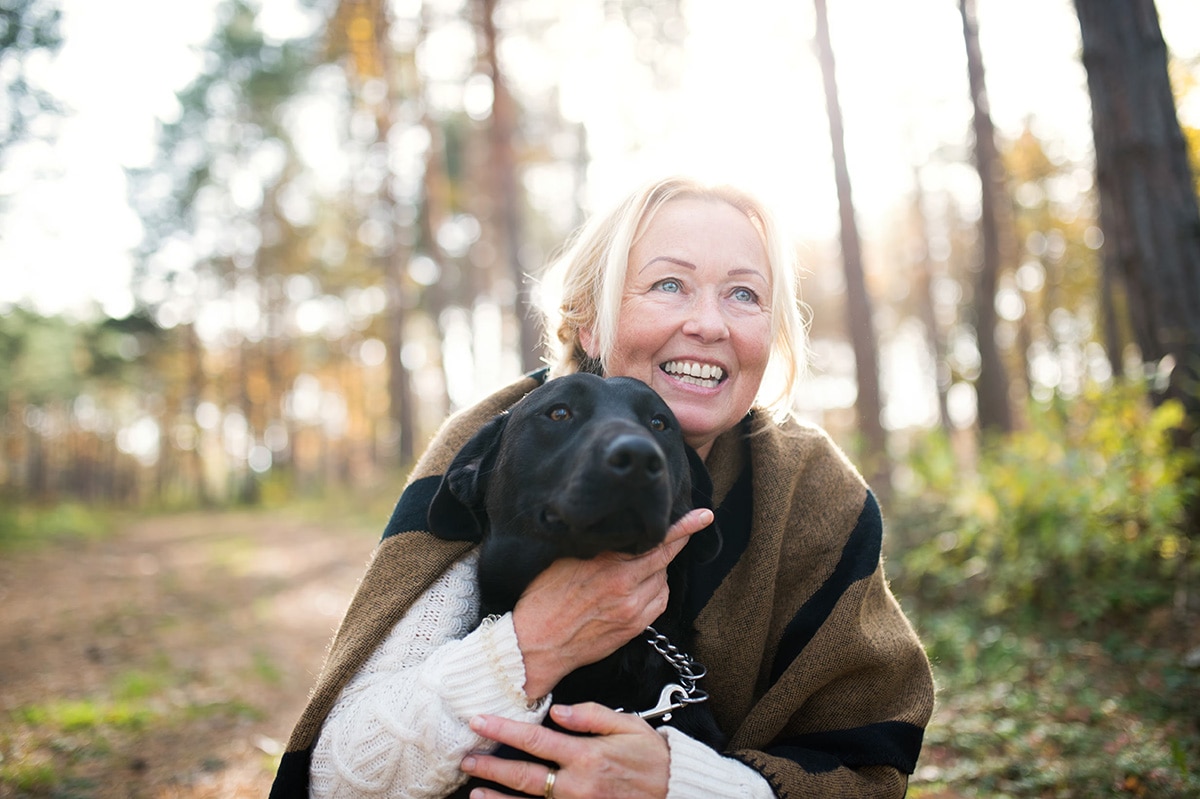 A blonde woman with a black dog in the woods
